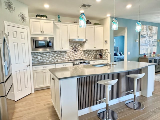 kitchen with stainless steel appliances, light wood-style floors, a sink, and under cabinet range hood