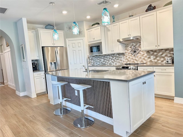 kitchen with visible vents, arched walkways, appliances with stainless steel finishes, under cabinet range hood, and a sink