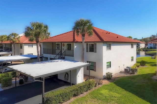 back of house featuring a carport, a water view, a yard, and central air condition unit