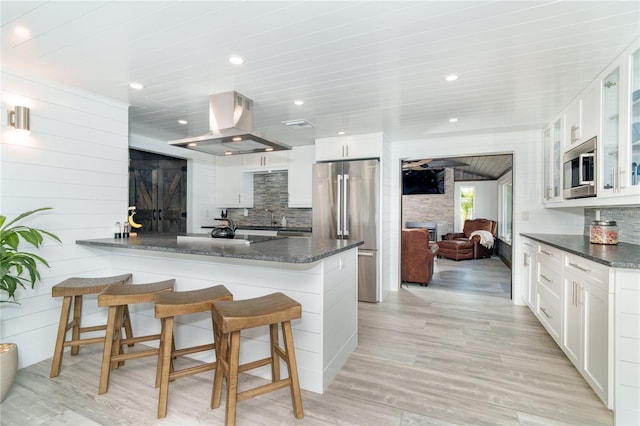 kitchen with island exhaust hood, dark stone counters, light wood-type flooring, white cabinetry, and appliances with stainless steel finishes