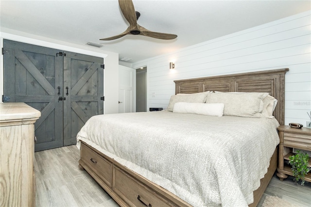 bedroom featuring wooden walls, a barn door, light wood-type flooring, and ceiling fan