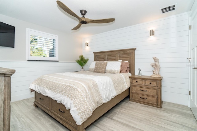 bedroom with wooden walls, light wood-type flooring, and ceiling fan