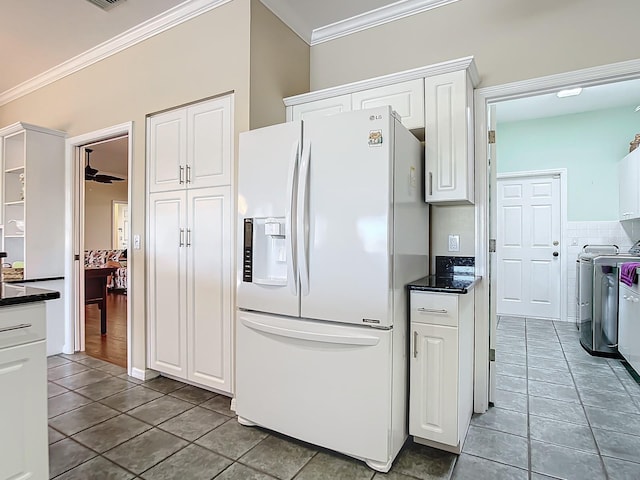 kitchen featuring white fridge with ice dispenser, washing machine and dryer, ornamental molding, and white cabinets