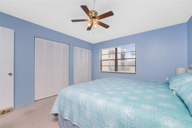 bedroom featuring light carpet, two closets, and ceiling fan