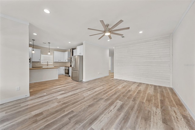 unfurnished living room featuring sink, crown molding, light wood-type flooring, and ceiling fan