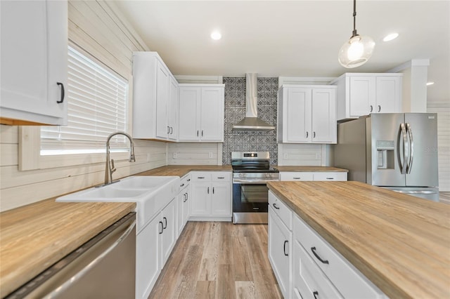 kitchen with wall chimney range hood, white cabinets, stainless steel appliances, and hanging light fixtures