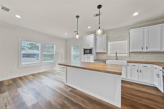 kitchen with white cabinets, stainless steel microwave, sink, and wooden counters