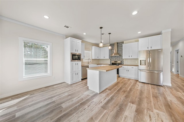 kitchen with butcher block counters, stainless steel appliances, a center island, decorative light fixtures, and white cabinetry