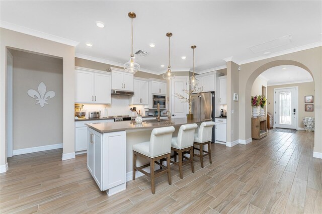 kitchen featuring light wood-type flooring, a kitchen island with sink, pendant lighting, and white cabinetry