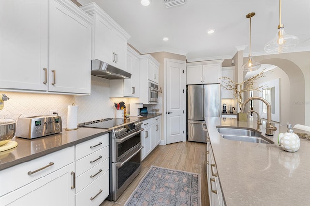 kitchen with high end appliances, white cabinetry, hanging light fixtures, and light wood-type flooring