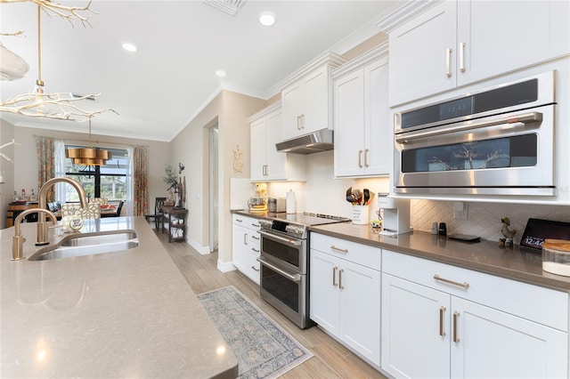 kitchen with sink, stainless steel appliances, pendant lighting, white cabinets, and light hardwood / wood-style flooring