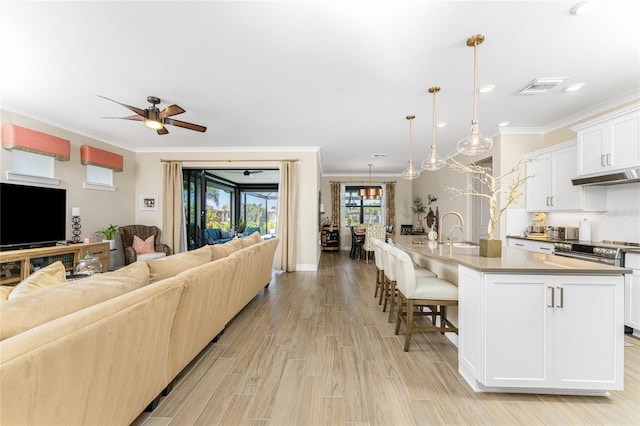 living room featuring ornamental molding, sink, light wood-type flooring, and ceiling fan