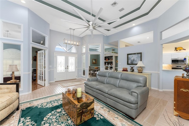 living room featuring french doors, light hardwood / wood-style flooring, ceiling fan with notable chandelier, and a high ceiling