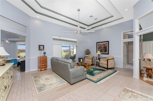 living room with a tray ceiling, a high ceiling, and ceiling fan