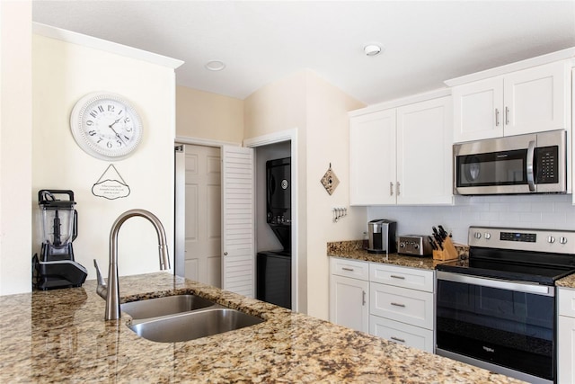 kitchen featuring white cabinetry, stacked washer / drying machine, appliances with stainless steel finishes, and light stone countertops