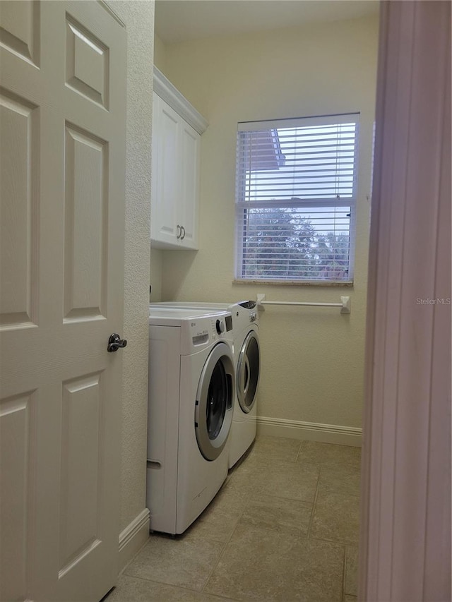 laundry room featuring washing machine and clothes dryer, light tile patterned floors, and cabinets