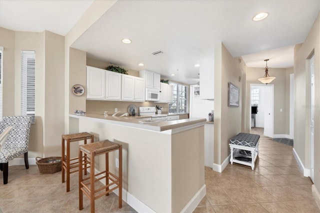 kitchen with kitchen peninsula, a breakfast bar, white appliances, white cabinetry, and hanging light fixtures