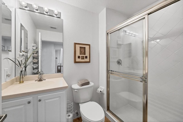 bathroom featuring a textured ceiling, vanity, toilet, and a shower with shower door