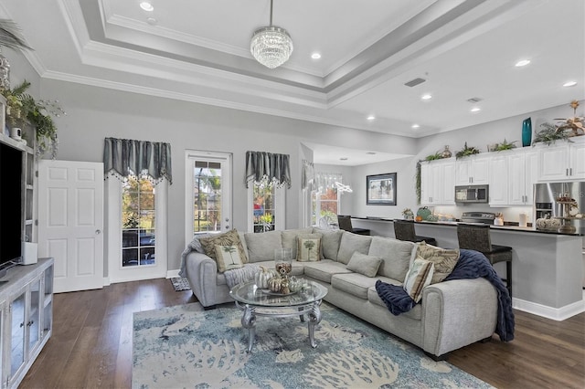 living room featuring dark wood-type flooring, a notable chandelier, ornamental molding, and a tray ceiling