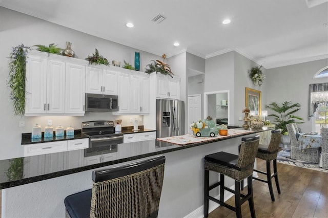 kitchen featuring dark hardwood / wood-style floors, dark stone counters, crown molding, white cabinetry, and appliances with stainless steel finishes