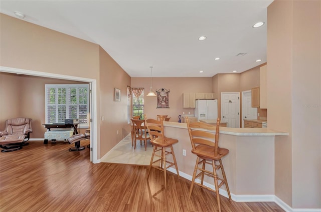 kitchen with a breakfast bar, kitchen peninsula, white refrigerator with ice dispenser, hanging light fixtures, and light hardwood / wood-style flooring