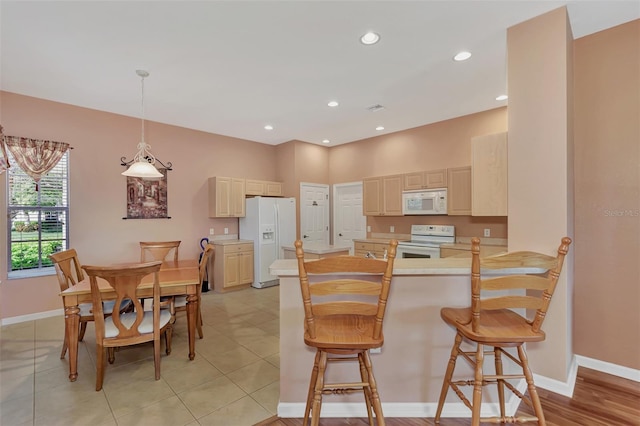 kitchen featuring light tile patterned flooring, kitchen peninsula, a kitchen bar, white appliances, and pendant lighting