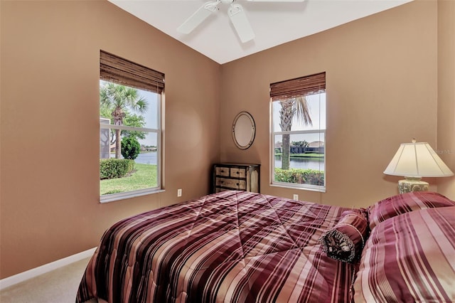 carpeted bedroom with a water view, multiple windows, and ceiling fan