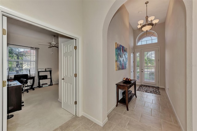 foyer featuring a high ceiling, light colored carpet, and ceiling fan with notable chandelier