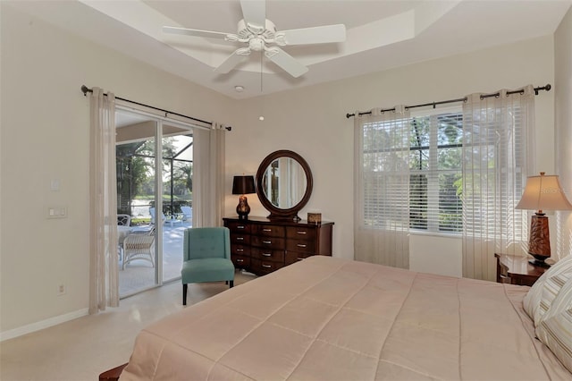 carpeted bedroom featuring ceiling fan, access to exterior, and a tray ceiling