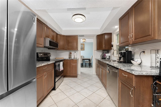 kitchen with sink, a raised ceiling, appliances with stainless steel finishes, light stone counters, and a textured ceiling