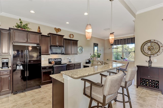 kitchen with a kitchen breakfast bar, an island with sink, backsplash, black appliances, and decorative light fixtures