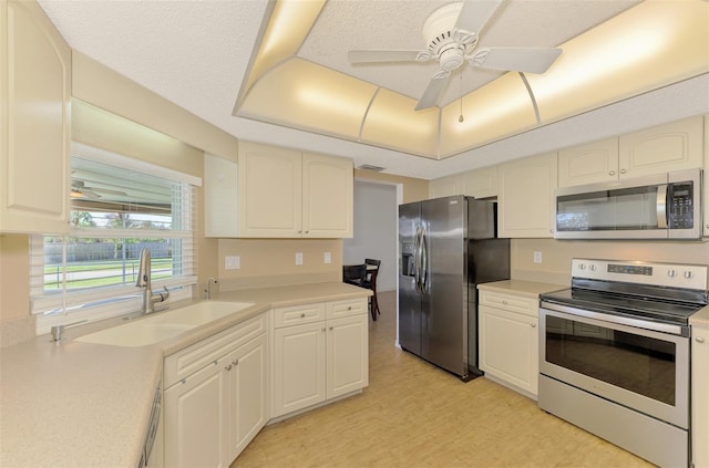 kitchen featuring a raised ceiling, appliances with stainless steel finishes, ceiling fan, a textured ceiling, and sink