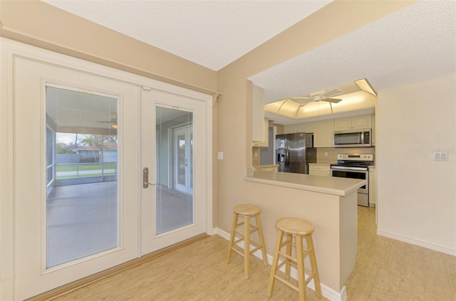 kitchen featuring kitchen peninsula, ceiling fan, appliances with stainless steel finishes, a breakfast bar area, and light wood-type flooring