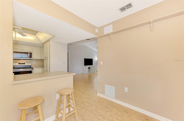 kitchen featuring a kitchen breakfast bar, kitchen peninsula, stainless steel appliances, a textured ceiling, and ceiling fan