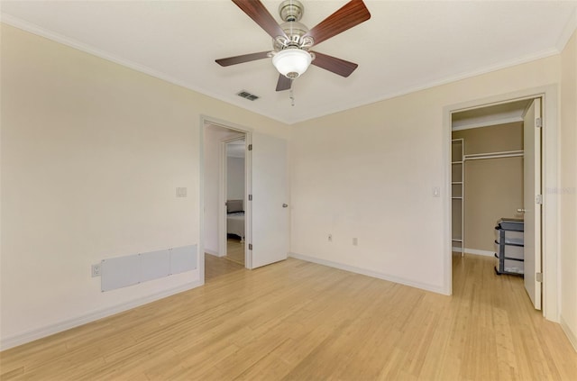 unfurnished bedroom with ceiling fan, light wood-type flooring, crown molding, a closet, and a walk in closet