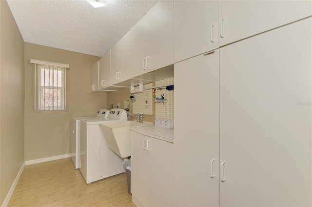 laundry room with cabinets, a textured ceiling, washing machine and clothes dryer, and light hardwood / wood-style floors