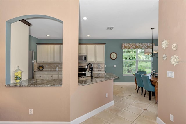 kitchen featuring tasteful backsplash, hanging light fixtures, stainless steel appliances, light stone counters, and a notable chandelier