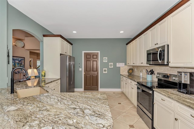 kitchen featuring sink, stainless steel appliances, light stone counters, decorative backsplash, and light tile patterned floors