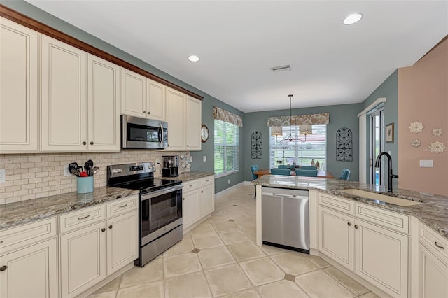 kitchen featuring hanging light fixtures, stainless steel appliances, sink, and cream cabinetry