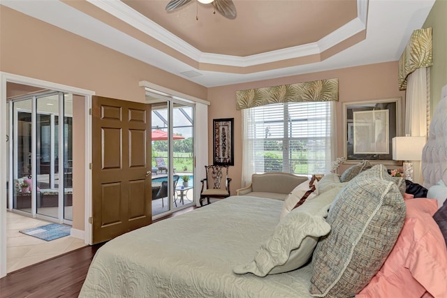 bedroom with ceiling fan, access to exterior, a tray ceiling, dark hardwood / wood-style floors, and crown molding