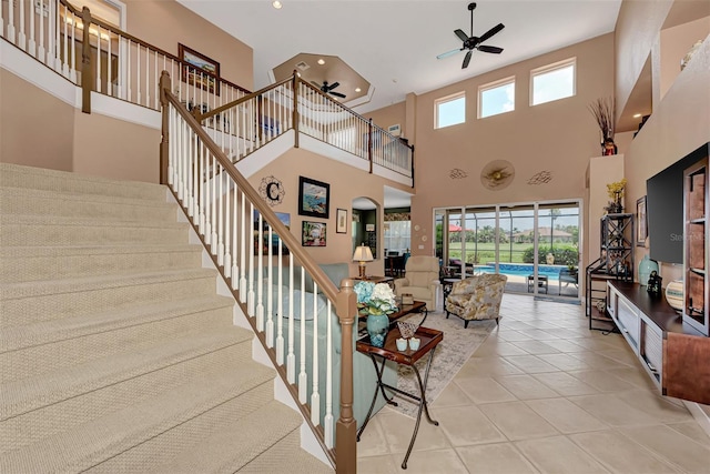 stairway featuring a towering ceiling, tile patterned flooring, ceiling fan, and a wealth of natural light