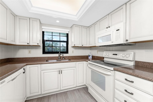 kitchen with white cabinets, a raised ceiling, light wood-type flooring, sink, and white appliances