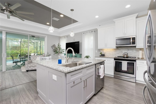 kitchen featuring appliances with stainless steel finishes, sink, white cabinets, light hardwood / wood-style flooring, and a center island with sink