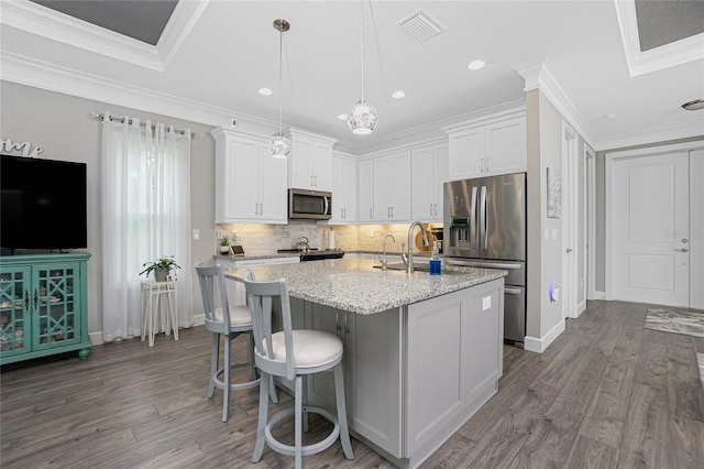 kitchen with stainless steel appliances, a center island with sink, crown molding, light stone countertops, and white cabinetry