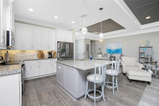 kitchen featuring light wood-type flooring, white cabinetry, stainless steel appliances, decorative light fixtures, and a center island with sink