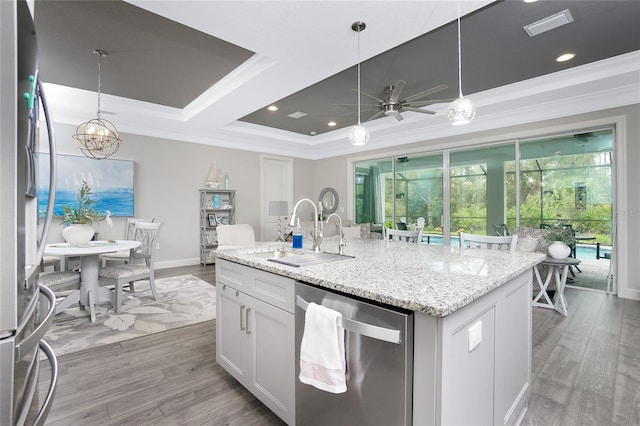 kitchen featuring an island with sink, hardwood / wood-style floors, decorative light fixtures, appliances with stainless steel finishes, and ceiling fan with notable chandelier