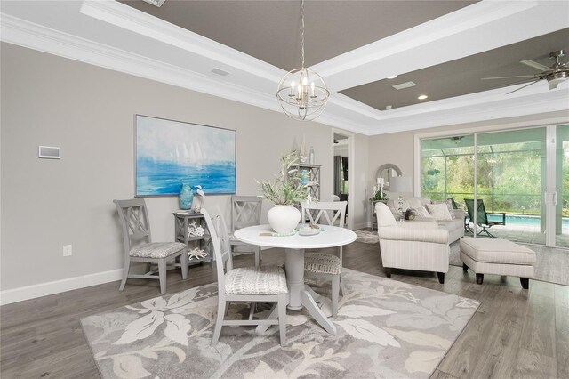 dining room with ornamental molding, hardwood / wood-style floors, ceiling fan with notable chandelier, and a raised ceiling