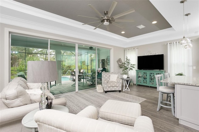 living room with ornamental molding, hardwood / wood-style floors, a raised ceiling, and ceiling fan