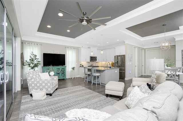 living room with dark wood-type flooring, sink, a tray ceiling, and ceiling fan with notable chandelier