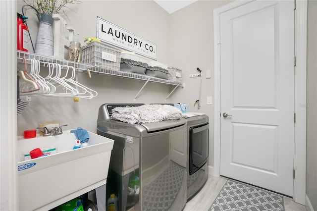 laundry area with light hardwood / wood-style floors, washing machine and dryer, and sink